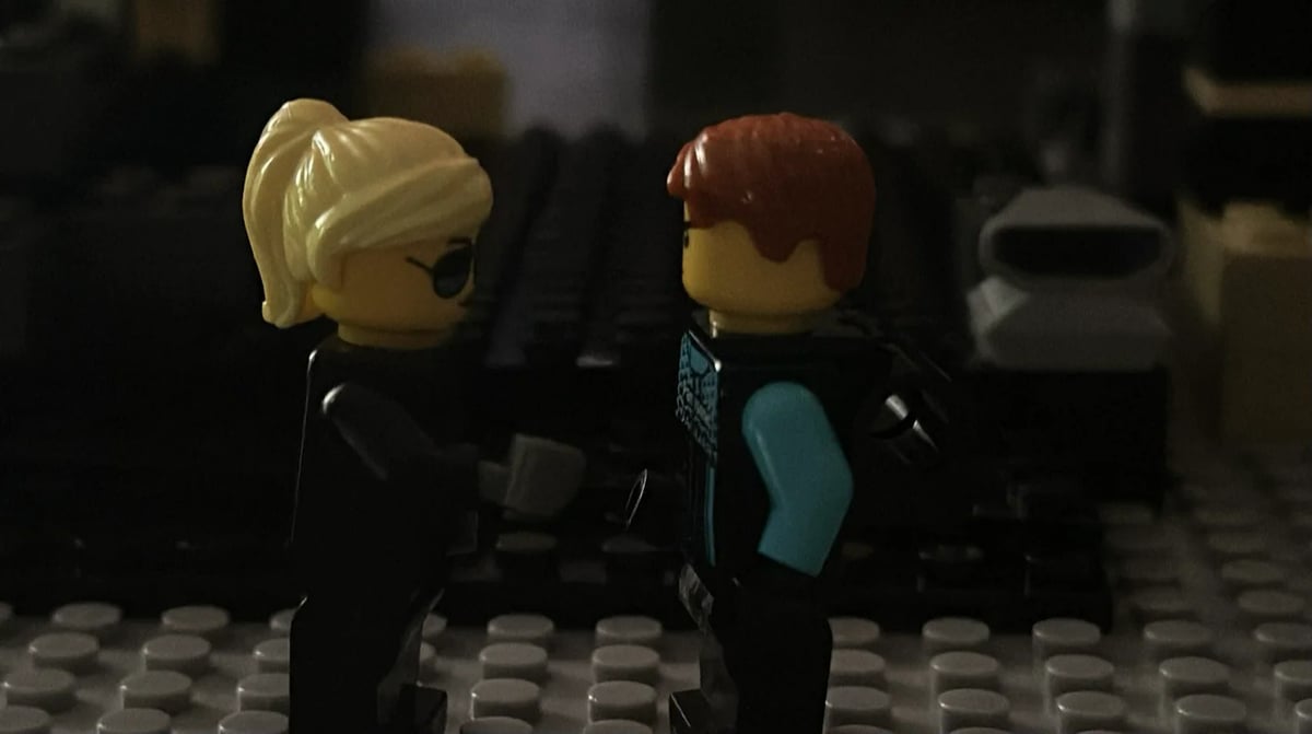 Two LEGO minifigures facing each other in a dimly lit scene with rows of LEGO studs in the foreground.