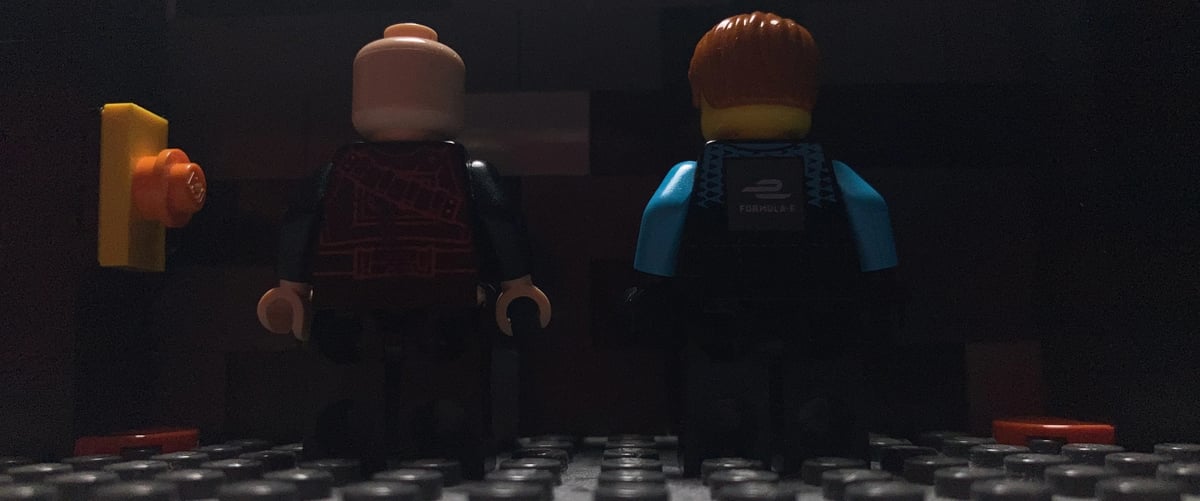 Two small LEGO-like figures stand facing away in a dark room with scattered items on the floor.