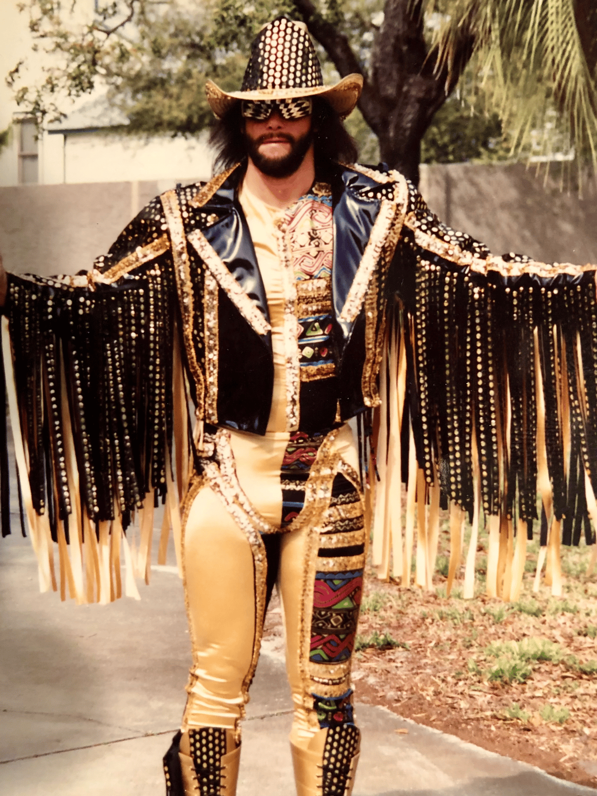 Bearded man in an elaborate black and gold fringed cowboy costume and decorative hat poses outdoors