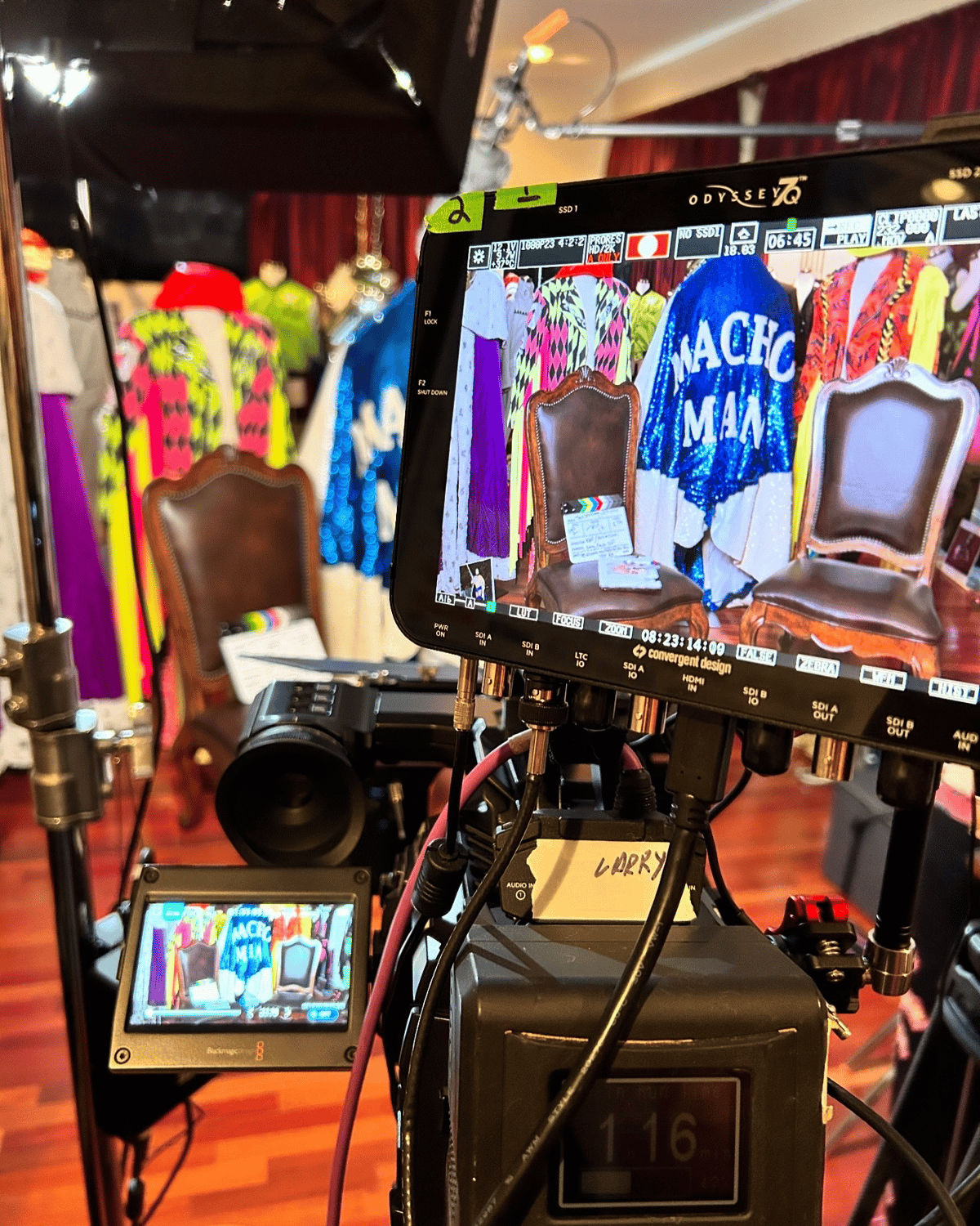 Cinema camera and monitor showing colorful costumes and chairs on a theatrical film set