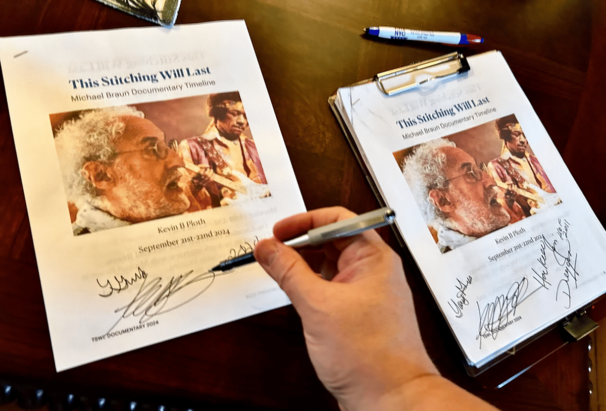 Hand signing two printed film poster copies featuring portraits and handwritten autographs on a wooden table.