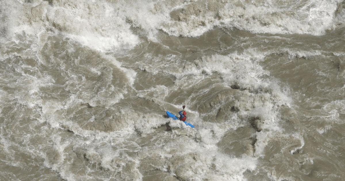 Aerial view of a person in blue and red gear surrounded by turbulent whitewater