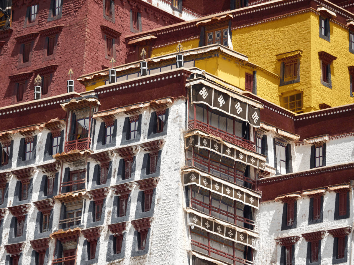 Ornate traditional building facade with red, yellow, and white walls, carved windows, and decorative balconies under bright daylight.