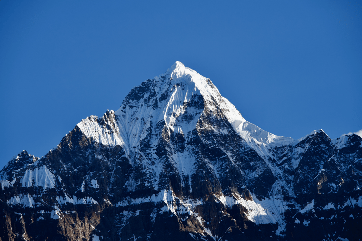 Snow-covered mountain peak rising above rugged dark ridges beneath a clear deep-blue sky