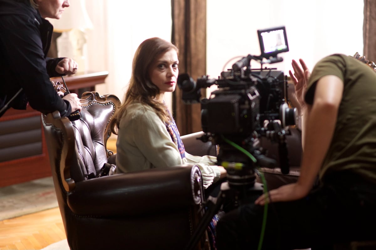 Camera crew filming an actress indoors, with professional lighting and a woman seated in a silver chair.