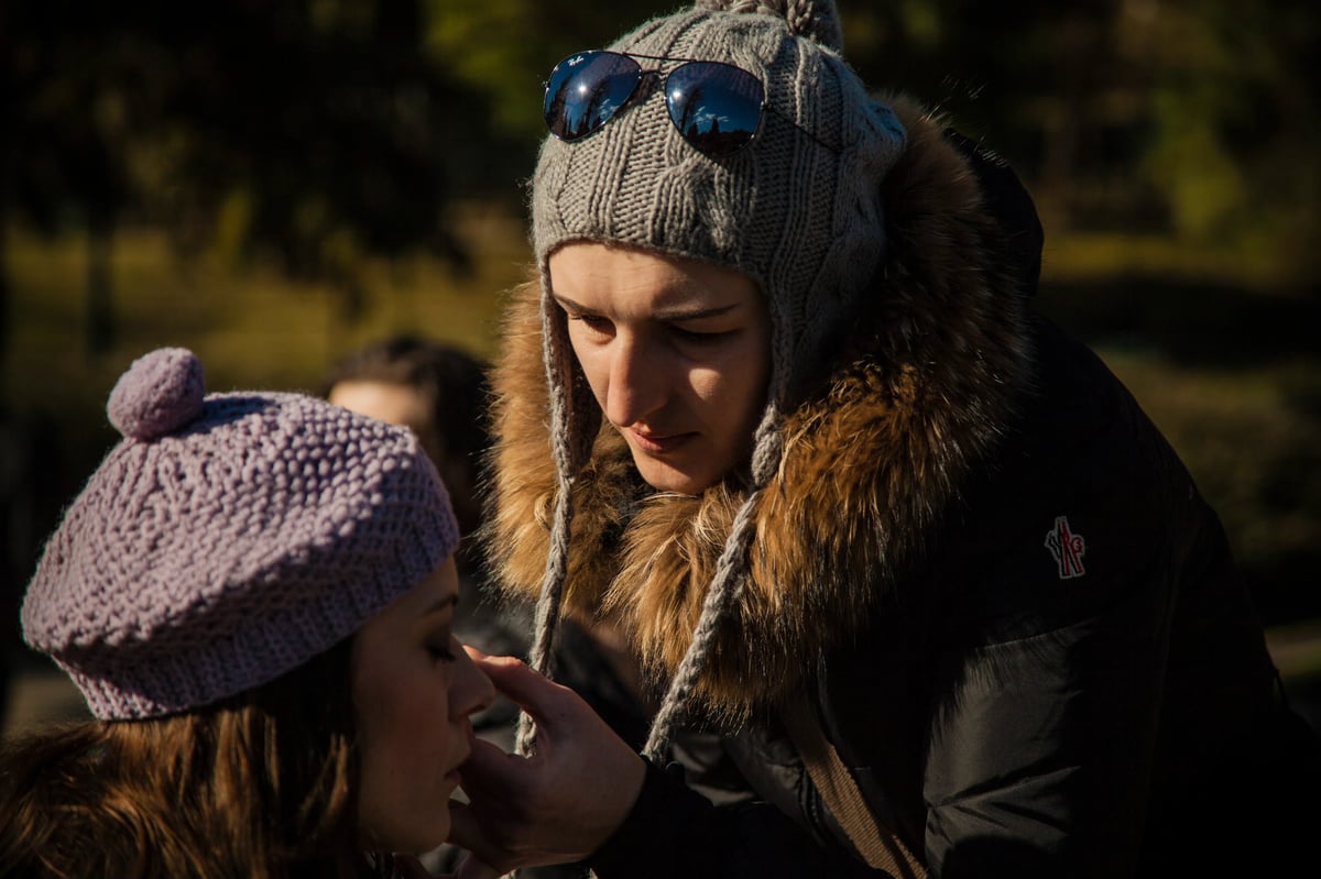 A woman in winter clothing with sunglasses looks down at a bundled child wearing a knit hat outdoors.