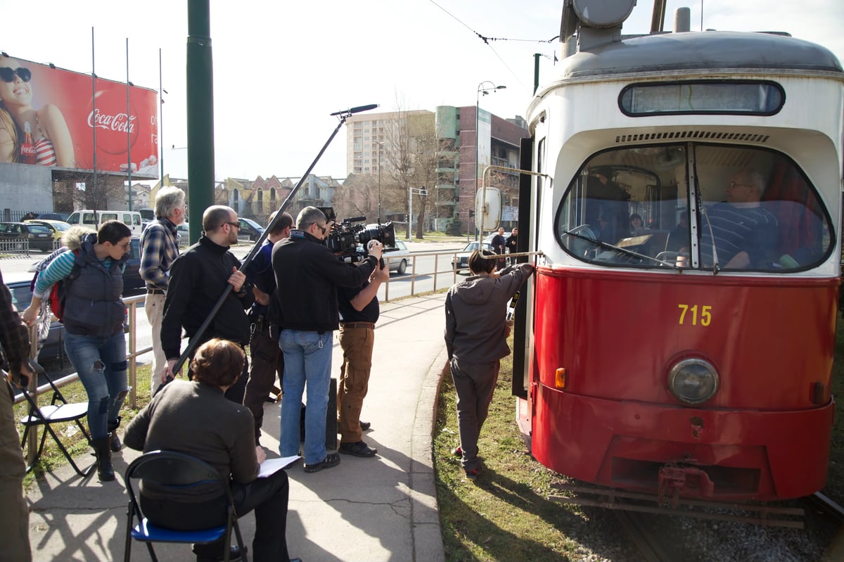 Film crew filming beside a red tram, with camera equipment set up near the vehicle and crew members watching the shot.