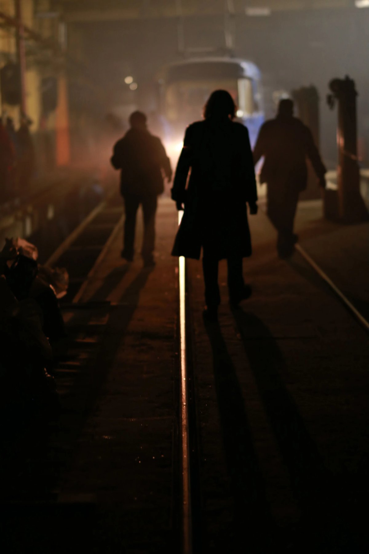 Silhouetted people walking through a dim, hazy hallway at night, framed by warm light.