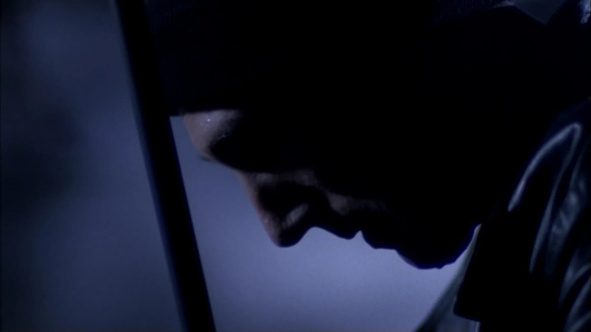 Close-up of a shadowed face in a dim blue-lit environment, partially obscured by darkness.
