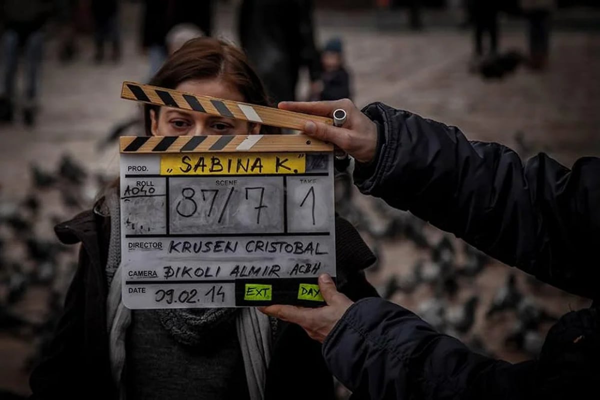 Person holding a clapperboard on a film set with a blurred audience behind.