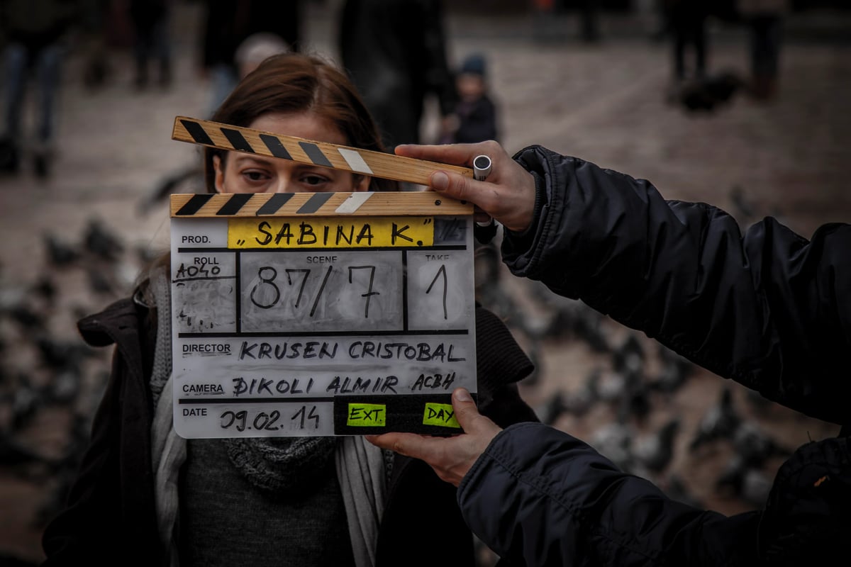 Close-up of a film clapperboard being held by a person, with another crew member blurred behind.