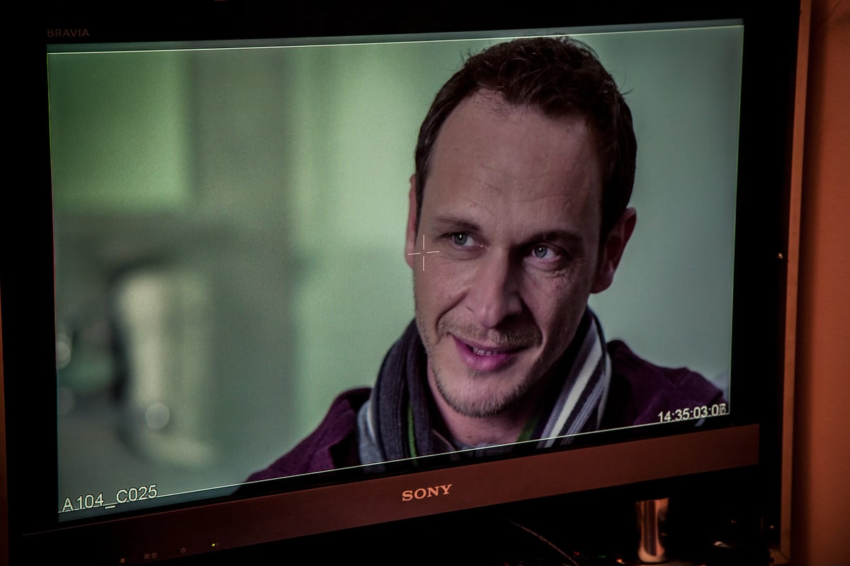Close-up portrait of a man shown on a monitor screen during filming, with camera recording overlay markings.