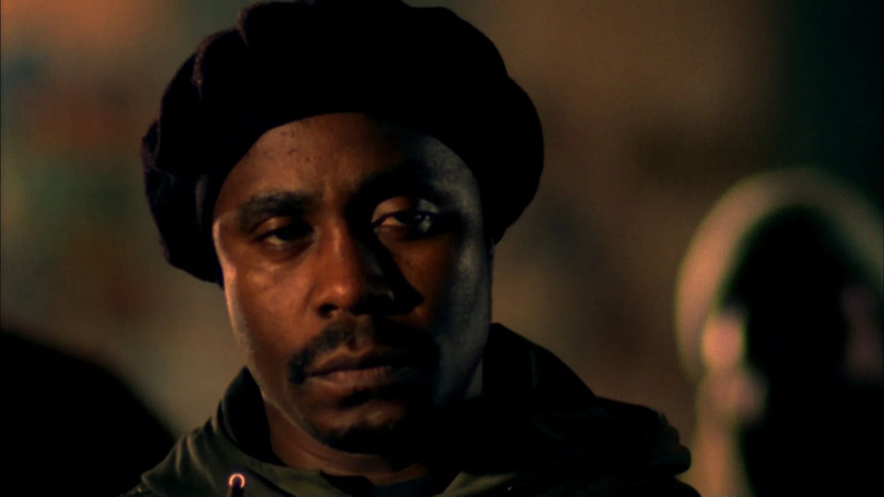 Moody close-up of a man wearing a dark beanie, lit warmly indoors.