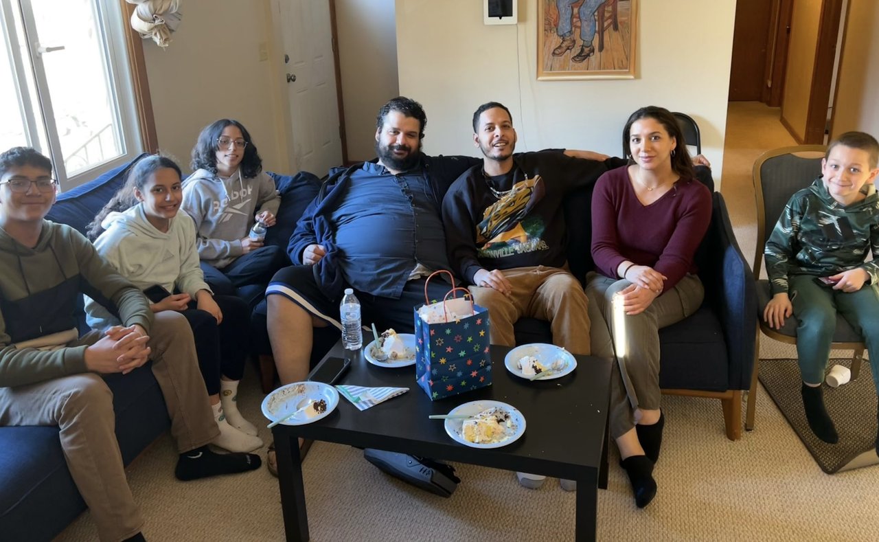 A group of seven people sitting in a living room for a casual celebration, with plates and snacks on a coffee table.